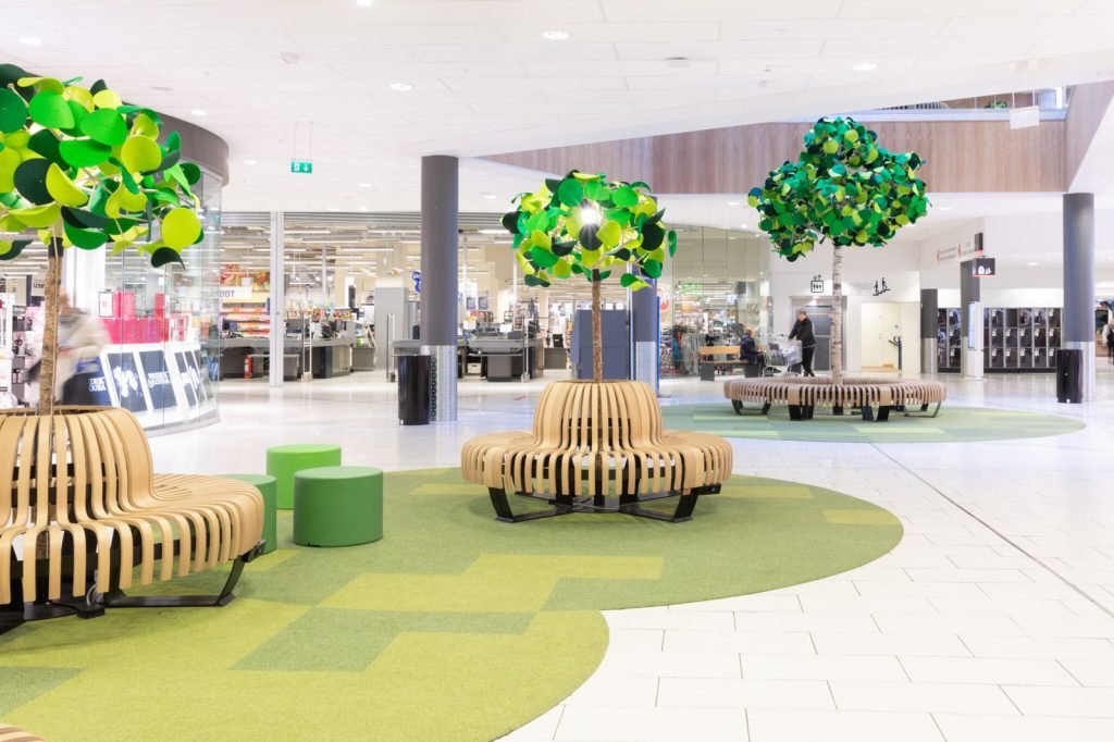Publikumsareal på Jekta med skulpturelle trær i grønt og blått over runde trebenker.